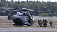 Ein verwundeter Soldat wird von vier Kameraden zu einem mit laufenden Rotoren wartenden Militärhubschrauber getragen.