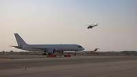 Ein weißes Flugzeug in Querfahrt und ein Hubschrauber der afghanischen Nationalarmee fliegt darüber