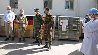 Vier Männer, davon drei in Uniform, stehen vor den Materialkisten. Rechts steht ein afghanischer Arzt mit Kittel und Haube