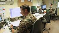 Eine Soldatin und ein Soldat sitzen in einem Büro und arbeiten am Computer, zwischen ihnen ist ein weiterer Computerplatz frei