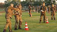 Mehrere Soldaten stehen auf dem Rasen hintereinander und transportieren im flachen Aufsatz des Feldessgeschirrs Wasser.