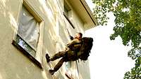 Ein Soldat mit Rucksack und Mund-Nasenschutz seilt sich von einem Gebäude ab.