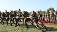 Mehrere Soldaten ziehen an einem Tau. Kameraden im Hintergrund feuern sie an.