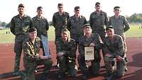 Die zehn Soldaten der Siegermannschaft auf der Tartanbahn eines Sportplatzes: Einer hält den Pokal, ein anderer die Urkunde.