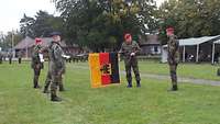 Ein Soldat hält die Truppenfahne. Ein weiterer befestigt ein Band an der Spitze der Truppenfahne.