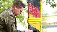 Ein Soldat hält einen Kompass an die Grenzsäule. So prüft er, ob der Betonpfahl nach Ost und West ausgerichtet ist