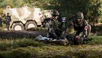 Two medics provide medical care to a casualty in front of a MRAV Boxer