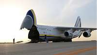 Auf einer Betonfläche steht die Antonov mit aufgeklappter Nase. Im Hintergrund sinkt die Sonne unter den Horizont