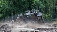 Ein Panzer fährt durch ein schlammbedecktes Areal auf einem Übungsplatz.