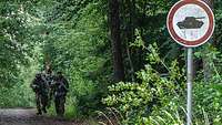 Drei Soldaten laufen einen dicht umwachsenen Waldweg entlang.