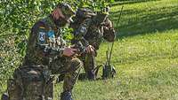 Zwei Soldaten hocken im Gelände. Sie bedienen verschiedene Funkgeräte.