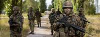 Mehrere bewaffnete Soldaten bewegen sich im Gelände.