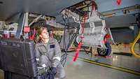 Eine Waffenmechanikerin kniet an einem Eurofighter vor einer Kiste mit technischen Geräten.