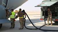 Vier Soldaten mit ausgerolltem Tankschlauch neben dem A400M, rechts ein Tankwagen 