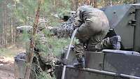 Zwei Soldaten betanken im Wald einen Kampfpanzer mit Betriebsstoff