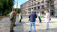 Mehrere Menschen stehen in einem großen Kreis vor einem eingerüsteten Rohbau