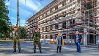 Mehrere Menschen stehen mit weitem Abstand zueinander vor einem eingerüsteten Rohbau