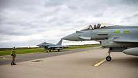 Gemeinsamer Flugbetrieb in Ämari Ein britischer und ein deutscher Eurofighter rollen gemeinsam auf dem Flugplatz in Ämari. Ein Einwinker weist den Jets den Weg.