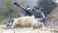 Zwei Soldaten fahren mit ihrem Panzer durch ein großes Wasserloch.