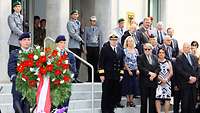 Zwei Uniformierte tragen einen Ehrenkranz zum Gedenkstein. Im Hintergrund stehen geladene militärische und zivile Ehrengäste