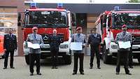 Drei Soldaten und fünf Feuerwehrmänner stehen mit ihren Urkunden vor zwei Einsatzfahrzeugen der Feuerwehr.