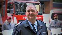Ein Feuerwehrmann schaut in die Kamera, hinter ihm stehen zwei Soldaten mit Urkunden in den Händen.