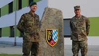 Zwei Soldaten stehen neben einem Findling mit dem Brigadewappen vor dem Stabsgebäude.