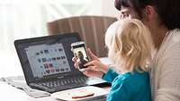 Mutter sitzt mit Kind am Tisch und führt ein Videotelefonat per Smartphone mit ihrem Mann, der sich im Einsatz befindet.