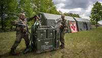 Two soldiers load boxes of material in front of a mobile aid station.