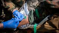 Close-up: A soldier inserts an IV catheter into a soldier’s upper arm.