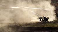 In dust whipped up by the rotor blades, soldiers carry a casualty to a helicopter waiting on the ground.