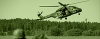 An NH90 helicopter hovers closely above a field.