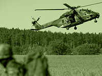 An NH90 helicopter hovers closely above a field.