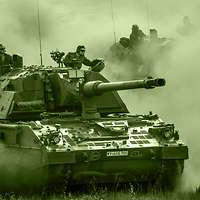 Two armoured self-propelled howitzers drive at speed, one behind the other, across a training area, whirling up dust.