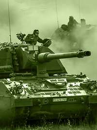 Two armoured self-propelled howitzers drive at speed, one behind the other, across a training area, whirling up dust.