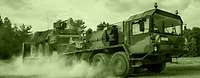 Army logistics personnel provide the force Raising a cloud of dust, a heavy equipment transporter carries a Fuchs armoured transport vehicle.