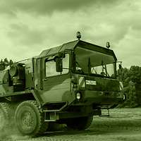 Raising a cloud of dust, a heavy equipment transporter carries a Fuchs armoured transport vehicle.