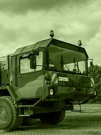 Army logistics personnel provide the force Raising a cloud of dust, a heavy equipment transporter carries a Fuchs armoured transport vehicle.