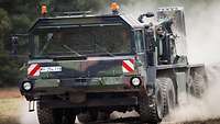 A heavy equipment transporter drives along a dirt road, raising dust.