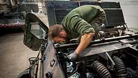 Using a flashlight, a serviceman inspects a vehicle’s engine compartment.