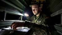 Using a flashlight, a serviceman searches a rack for a small spare part.