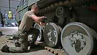 Kneeling down, a serviceman uses a crowbar on the running gear of a Marder infantry fighting vehicle.