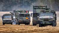 Several transport vehicles cross a harvested grain field.