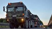 A heavy equipment transporter carrying an armoured self-propelled howitzer drives along a road. 