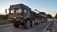 A heavy equipment transporter carrying an armoured self-propelled howitzer crosses a motorway bridge.