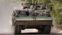 An armoured recovery vehicle rolls along a dusty road.