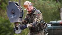 A serviceman controls the crane hook of an armoured recovery vehicle with both hands.
