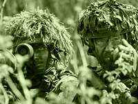 The image shows two armed infantry soldiers: A platoon leader is giving instructions to a soldier.