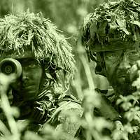 The image shows two armed infantry soldiers: A platoon leader is giving instructions to a soldier.