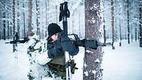 Two mountain infantrymen in winter camouflage provide security in snow-covered, wooded terrain.